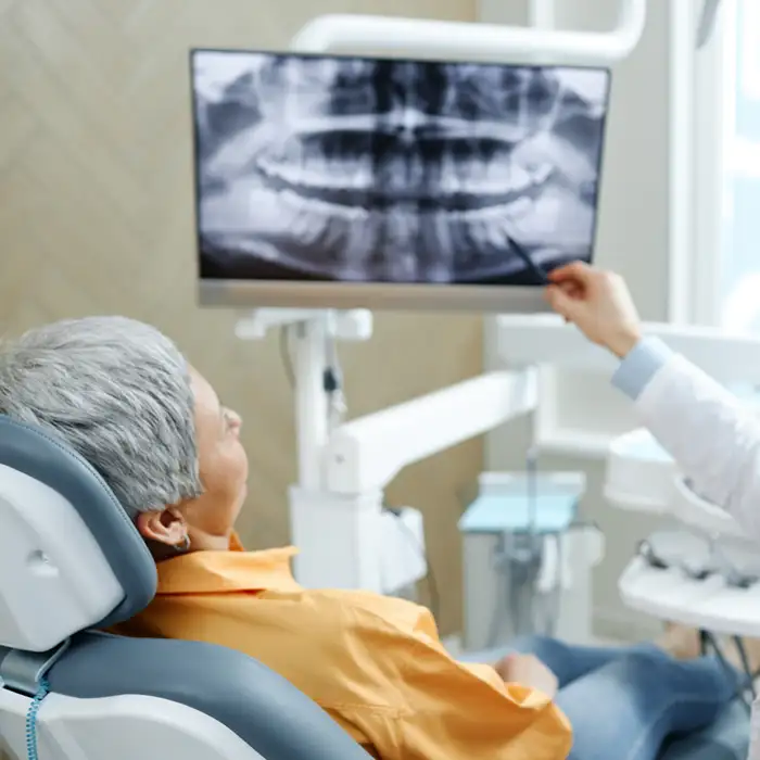 mature woman in a dentist's chair listening to oral surgeon discussing her x-ray